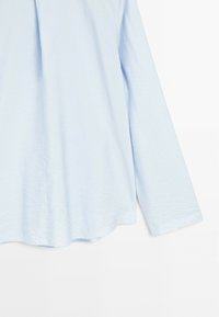 Chemise à manches longues bleu clair avec une coupe ample et une légère texture froissée, présentée sur fond blanc.