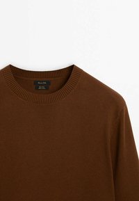 Bruine wollen trui met een geribbelde ronde hals, een gladde textuur en een label met merk- en verzorgingsinstructies. Geen versieringen of patronen.