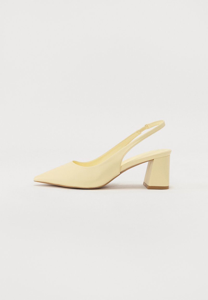 Sandal pump em bege com bico fino e salto bloco, acabamento suave e detalhe em faixa elástica contra um fundo liso.