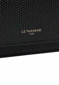 Portafoglio nero testurizzato con logo dorato embossato "LE TANNEUR 1898" sulla parte frontale. Il materiale presenta un motivo intrecciato e bordi lisci.