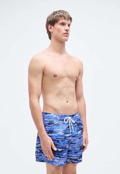 Μπλε μαγιό βερμούδα με κυματιστό μοτίβο σε διάφορες αποχρώσεις του μπλε, με λευκό κορδόνι και ελαφρύ, αεριζόμενο ύφασμα.