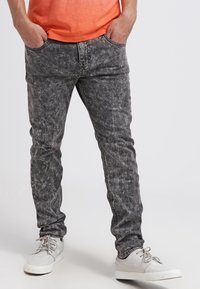 Šedé džíny z denimu s vybledlým, opotřebovaným vzhledem, slim fit a tradičním designem s pěti kapsami. Kombinované s bílými teniskami.