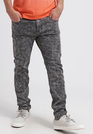 Jean en denim gris avec une texture décolorée et usée, coupe slim et design traditionnel à cinq poches. Associé à des baskets blanches.