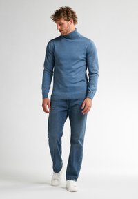 Suéter de cuello vuelto azul en tejido de punto suave, diseño ajustado, combinado con jeans azules y zapatillas blancas. Textura lisa, sin patrones visibles.