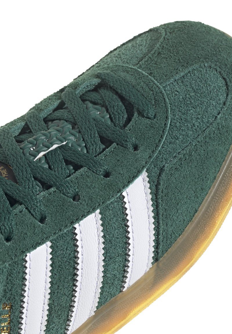 Sneaker verde in suede con strisce bianche, superficie testurizzata e suola in gomma. Presenta un design con lacci e cuciture rinforzate.