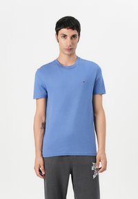 T-shirt en coton bleu avec un col rond et des manches courtes. Présente un petit logo rouge, blanc et bleu sur la poitrine. Texture douce.