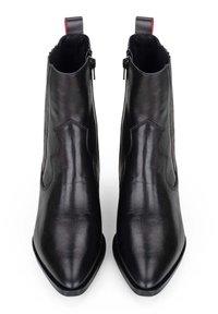 Botas de tobillo de piel negra con punta afilada, paneles laterales elásticos y un lazo rojo en el tacón. Textura suave con un detallado mínimo.