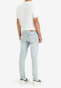 Bílý tričko s krátkým rukávem, světle modré zúžené džíny se zadními kapsami, hnědá kožená nášivka a černobílé tenisky.