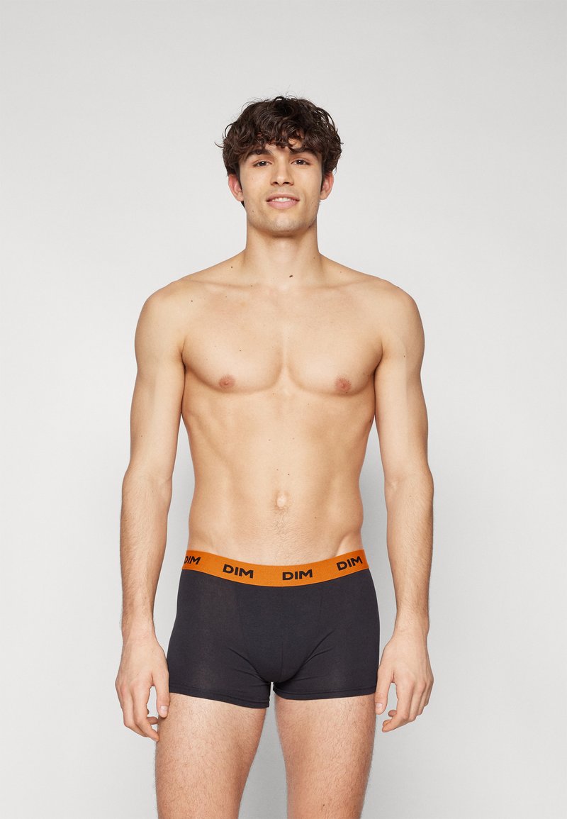 Svarte boxershorts med en oransje DIM-logo på midjebåndet, laget av et glatt stoff, med en tettsittende design og kort benlengde.