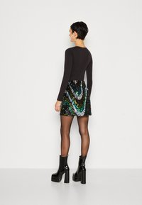 Haut à manches longues noir associé à une mini-jupe à sequins multicolores étincelants et des bottines à plateforme noires brillantes, mettant en avant une silhouette ajustée.