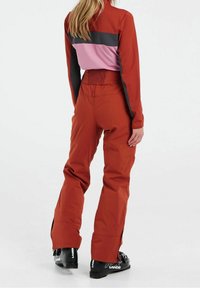Roter und rosa Skianzug mit einem taillierten Oberteil und lockeren Hosen. Verfügt über einen elastischen Bund und einen Reißverschluss an den Beinöffnungen. Das Material erscheint glatt und strapazierfähig.