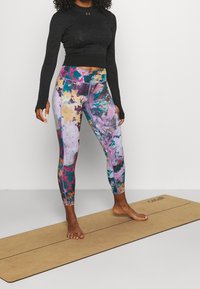 Svart långärmad topp kombinerad med flerfärgade leggings med abstrakta mönster. Leggings har livliga nyanser av rosa, blått och gult.