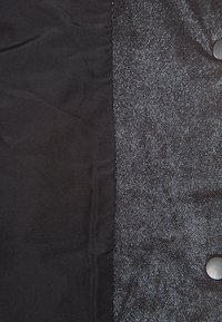 Tissu noir à texture mate à gauche et cuir noir texturé avec un éclat métallique et un bouton sur le côté droit.