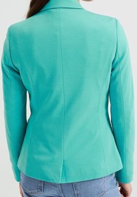 Stenturkos blazer med en slät textur, strukturerad design och en ventil i ryggen. Långa ärmar sträcker sig från en notch-krage.