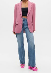Blazer rose à coupe ajustée, deux boutons et poches avant. Associé à un jean bleu à jambes larges et des chaussures plateforme roses vives.