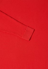 Top rosso a maniche lunghe con texture a coste, dotato di un ampio polsino alla fine di una manica. Il tessuto ha una finitura liscia e leggermente lucida.