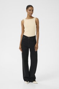 Top in riga beige con dettagli di borchie sulle spalle, abbinato a jeans neri a vita alta e gamba larga, e scarpe bianche a punta.