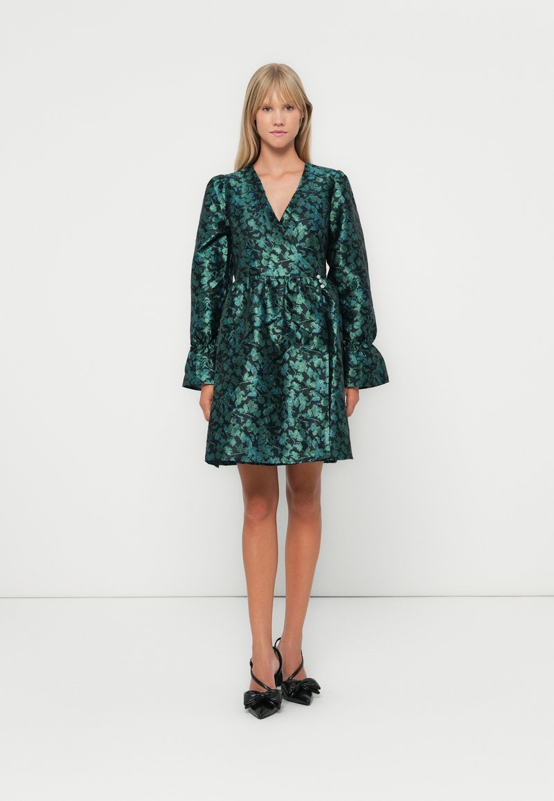 Green floral patterned dress with a V-neck, long puffed sleeves, and a cinched waist. Worn with black heeled sandals featuring bow accents.