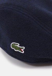 Navy blue felt cap featuring embroidered green crocodile logo with red accents, structured design, and visible stitching details.
