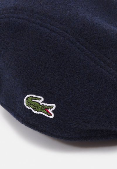 Casquette en feutre bleu marine ornée d'un logo de crocodile vert brodé avec des accents rouges, au design structuré et avec des détails de couture visibles.