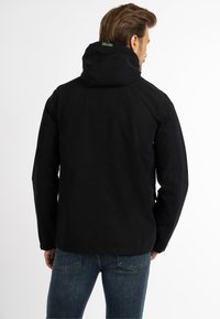 Fekete kapucnis dzseki, sima textúrával és minimalista dizájnnal. A hátsó részen címke látható a nyaknál és egyszerű varrások. Kék farmer nadrággal párosítva.