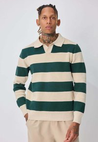 Pull rayé vert et crème avec un col, texture côtelée et manches longues, présentant une coupe décontractée et des détails de couture visibles.