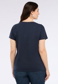 Námořnická modrá trička s krátkým rukávem a kulatým výstřihem, vyrobené z hladké bavlny, v kombinaci s tmavě modrými džínami. Minimalistický design bez vzorů.