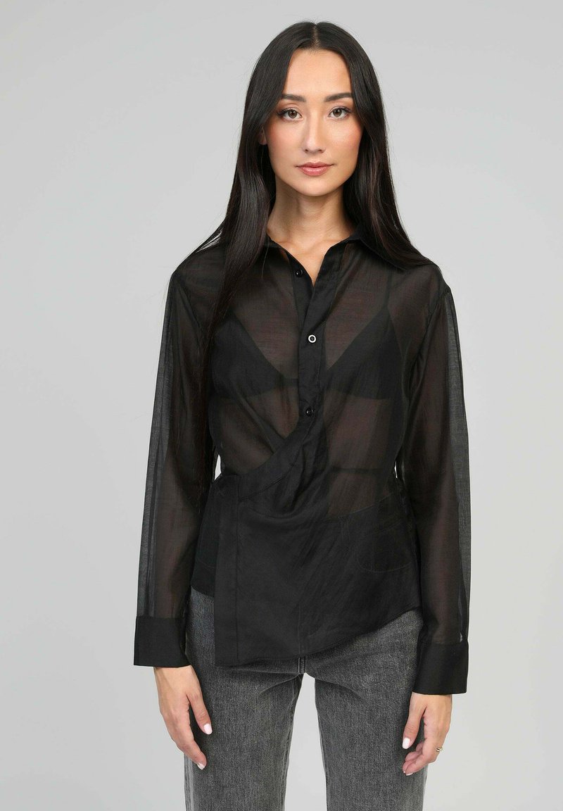 Blouse noire transparente à manches longues avec un col, des boutons à l'avant et un design asymétrique. Texture lisse et coupe décontractée.