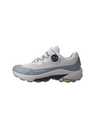 Hellgrauer und weißer Sportschuh mit schwarzem Drehverschluss-System, dicker Sohle und Vibram-Logo an der Außensohle, Seitenansicht.