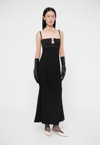 Melna kleita ar piegulošu korseti, caurspīdīgu paneļu un savilktu reljefu. Kombinēta ar melniem ādas cimdiem un krēmkrāsas kurpēm ar smailu purngalu.