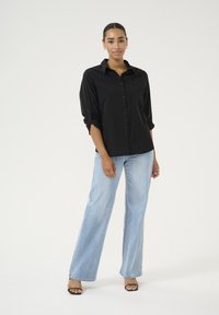 Chemise noire à boutons, avec les manches retroussées, assortie à un jean large bleu clair et des sandales noires. Ensemble simple, décontracté et au design épuré.