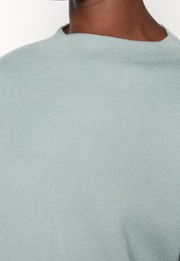 Hellblauer gestrickter Pullover mit hohem Kragen und glatter Textur, der ein einfaches, modernes Design ohne Verzierungen hervorhebt.
