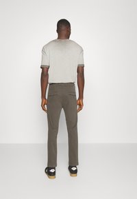 Grå kortärmad t-shirt med mörkgrå detaljer, i kombination med olivgröna byxor med bakfickor och svarta skor med vita logga accenter.