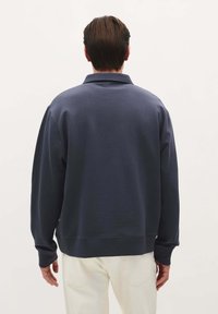 Navy blauwe pullover sweatshirt met een ontspannen pasvorm, voorzien van een kraag, verlaagde schouders en ribgebreide manchetten bij de mouwen en de taille.