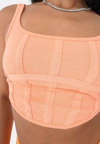 Gerippter Crop-Top in Pastellorange mit einem quadratischen Ausschnitt und vertikalen Nähten für Textur, mit dünnen Trägern und einer figurschmeichelnden Silhouette.