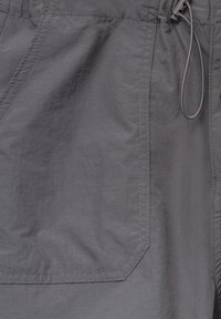 Tummanharmaa kangas, jossa on suuri neliömäinen tasku, jossa näkyvät ompeleet ja naruvalmius oikeassa yläkulmassa.