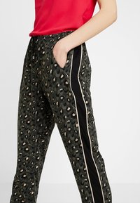 Joggingsbroek met luipaardprint in donker groen, met zwarte zijpanelen en crèmekleurige strepen. Beschikt over een elastische taille en zijzakken voor extra comfort.