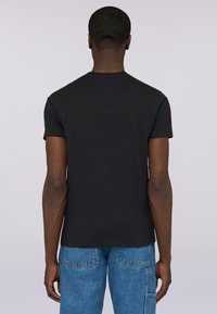 Czarna bawełniana koszulka z krótkimi rękawami, okrągłym dekoltem i prostym wzorem. Noszona z niebieskimi dżinsami, ukazująca widok z tyłu.