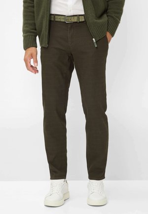 Olivgrüne Hosen mit geradem Schnitt, ausgestattet mit einem strukturierten Gürtel in passender Farbe und weißen Sneakers mit dicker Sohle.