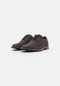 Brown lace-up shoes with a smooth texture, rounded toe shape, and contrasting light brown sole. Minimalist design with no visible patterns.