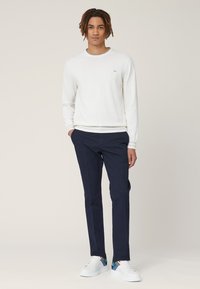 Wit sweatervest met ronde hals, marineblauwe chino's en witte sneakers met geometrische accenten. Casual outfit met gladde texturen en een getailleerd ontwerp.