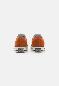 Oranžas kanvas kedas ar baltajiem kontrastējošajiem šuvēm un melno gumijas zoli, kas iezīmē "Converse All Star" zīmolu uz papēža.