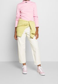 Nike rosa långärmad tröja med hög hals, gul tröja knuten runt midjan, vita cropped byxor och rosa sneakers med vita accenter.