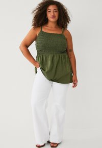 Olijfgroen tanktop met gerimpeld lijfje, dunne bandjes en een vloeiende onderkant, gecombineerd met witte wijde broekspijpen en bruine sandalen.