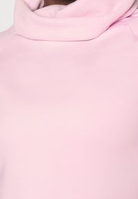 Close-up of a person wearing a light pink sweatshirt with a soft, fleece-lined cowl neck collar.