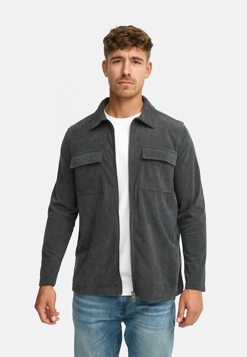 Grå kordfløjljakke med lynlåsfortil, to brystlommer og krave. Bæres over en hvid skjorte og kombineres med lyseblå jeans.