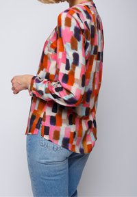 Blusa a maniche lunghe con un motivo astratto multicolore, che presenta tonalità di rosa, arancione e blu. Tessuto leggero con una vestibilità comoda.