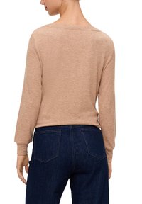 Beige trui met lange mouwen en een relaxte pasvorm, met een brede halslijn, gedragen met donkerblauwe jeans met twee achterzakken.
