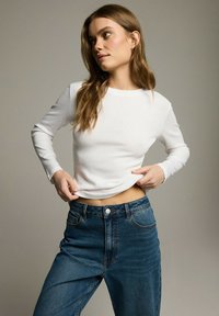 Biała bluzka z długim rękawem o prążkowanej teksturze, połączona z niebieskimi dżinsami z wysokim stanem, z zapięciem na guzik i kieszeniami bocznymi.