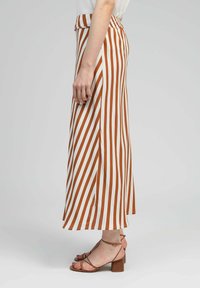 Jupe maxi rayée en blanc et rouille, dotée d'une taille haute et d'une silhouette fluide. Associée à des sandales à talons strappy marron.